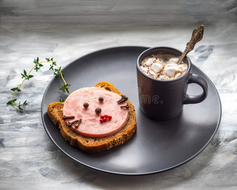 Breakfast with coffee and funny sandwich with sausage in the form of a cat`s face on a dark plate on a dark background in