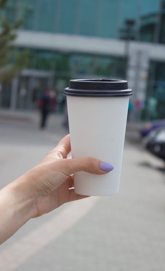 Breakfast and coffee theme: a woman`s hand holding a white paper coffee Cup with a black plastic lid