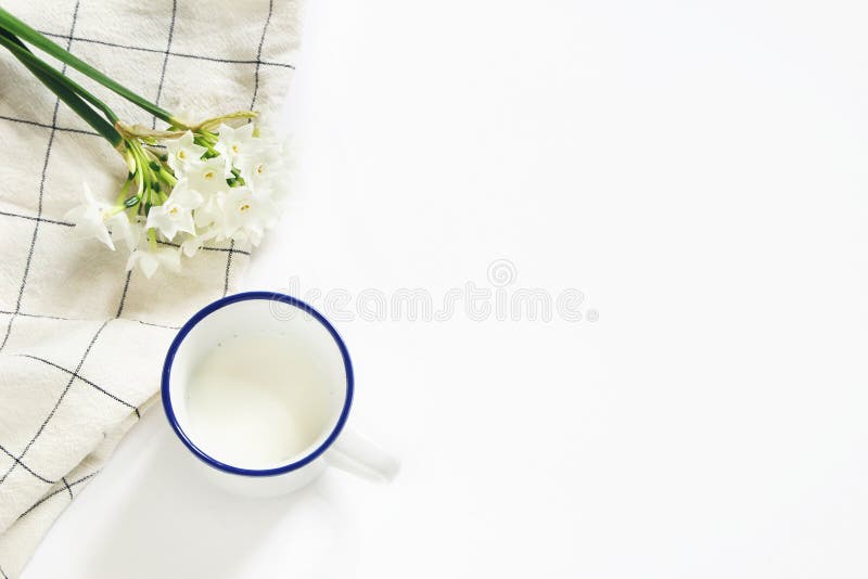 Breakfast scene with mug of milk, tea towel and bouquet of narcissus, daffodil flowers on white table background. Spring