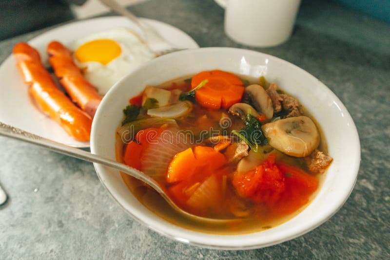 Breakfast Set of Fried Egg Sausages and Vegetable Soup Served on Table