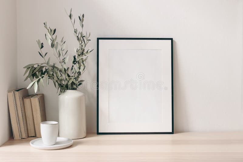 Breakfast still life. Cup of coffee, books and empty picture frame mockup on wooden desk, table. Vase with olive