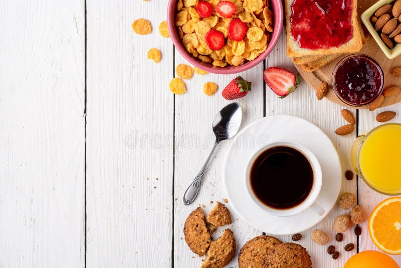 Breakfast table with healthy tasty ingredients. Coffee, toast, jam, corn flakes, cookies, almonds, orange juice and fruit on white