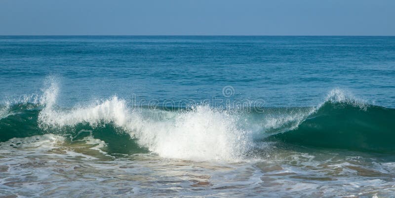 Breaking sea wave with stone on a sandy beach