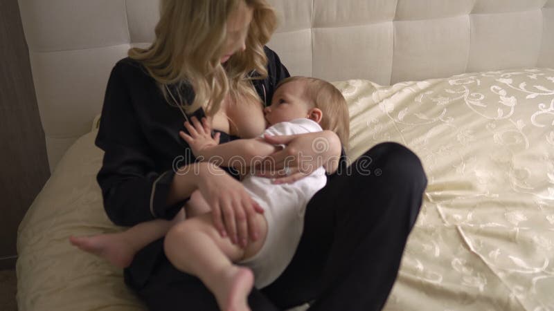 Breast Feeding: Young Blonde Mother Breastfeeds Her Baby Boy Child in Bedroom Wearing Black Sleeping Robe Costume - Son Stock Footage - Video of chair, home: 148573196