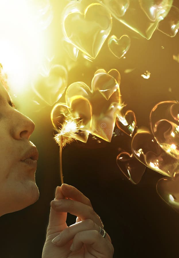 Woman blowing on a dandelion whose seed creates bubbles with the shape of hearts flying everywhere. Woman blowing on a dandelion whose seed creates bubbles with the shape of hearts flying everywhere.