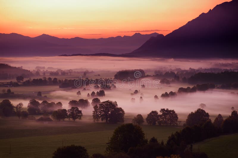 Breathtaking morning lansdcape of small bavarian village covered in fog. Scenic view of Bavarian Alps at sunrise with majestic mou