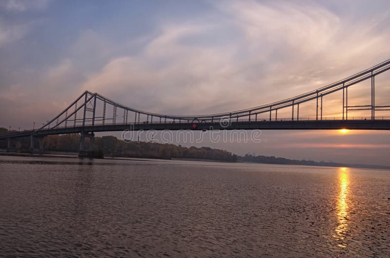 Bred vinkellandskappanorama av den Dnipro floden, invallningen och den fot- bron Färgrik vibrerande himmel, sol reflekterade i va arkivfoton Bred vinkellandskappanorama av den Dnipro floden, invallningen och den fot- bron Färgrik vibrerande himmel, sol reflekterade i va arkivfoton