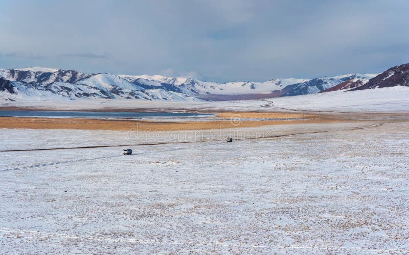 Wide winter steppe, a narrow road, cars driving across the plateau on a narrow dirt road. The wide winter Mongolian steppe. Wide winter steppe, a narrow road, cars driving across the plateau on a narrow dirt road. The wide winter Mongolian steppe.