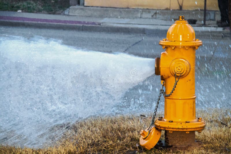 Breites Öffnen strömendes Wasser des gelben Hydranten auf die Straße mit körnigem Effekt, wo das Wasser unten über Defaults