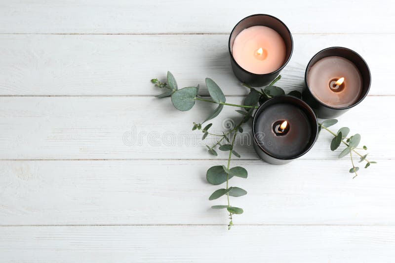 Brennende Kerzen und grüne Niederlassungen auf weißem Holztisch, flache Lage
