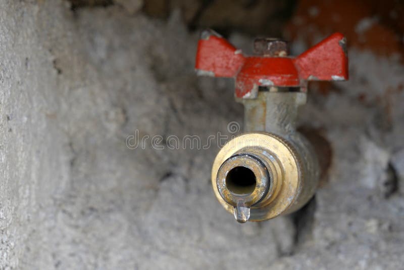Outdoor hose bib or hydrant  installed in wall. Il is leaking slightly and there is a drop of water just about to fall down. Copy space is on the left side of the photo. Outdoor hose bib or hydrant  installed in wall. Il is leaking slightly and there is a drop of water just about to fall down. Copy space is on the left side of the photo.