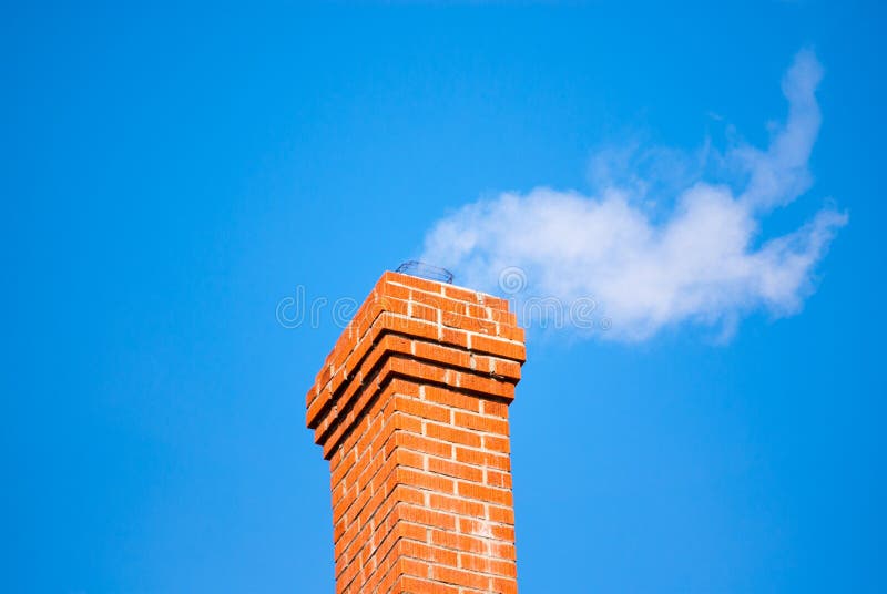 Brick chimney releasing smoke on sky.