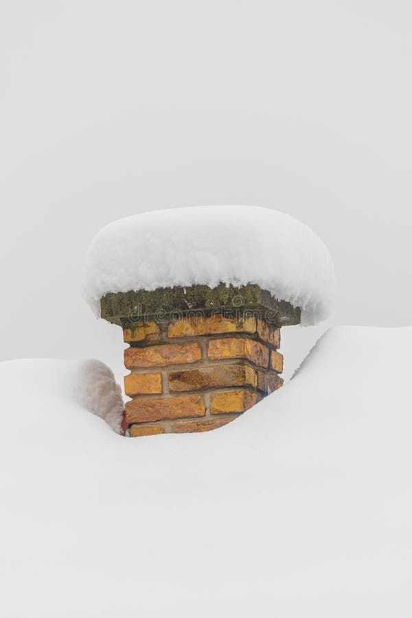 Brick chimney with a thick rounded snow cap protruding from a smooth deep snowdrift against a pale hazy sky stock photography