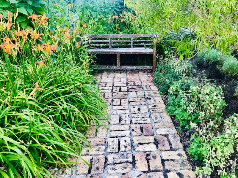 A brick walkway leads to an old garden bench.