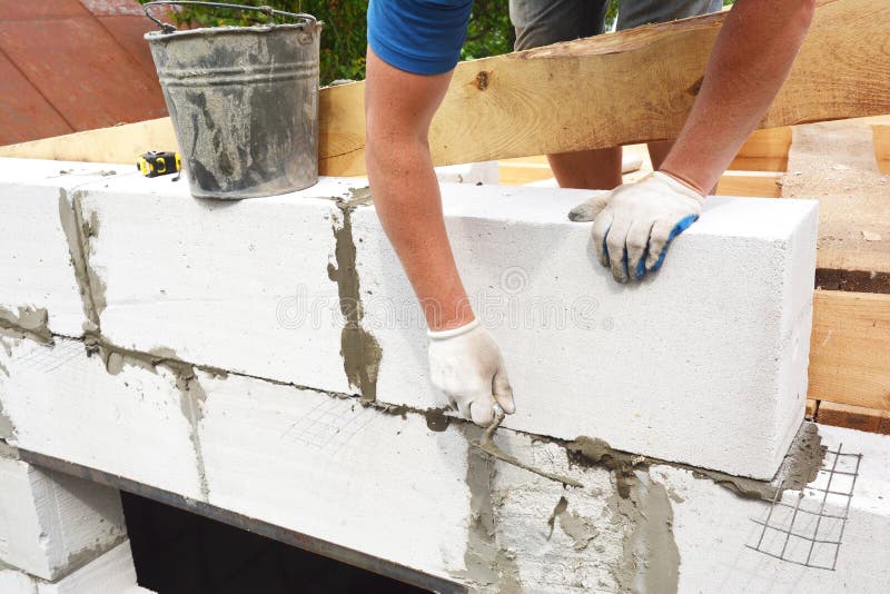 Bricklayer builder laying autoclaved aerated concrete blocks for house wall near unfinished roof wooden beams stock images Bricklayer builder laying autoclaved aerated concrete blocks for house wall near unfinished roof wooden beams stock images