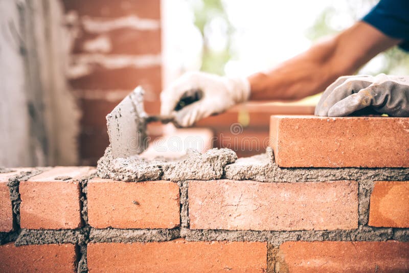 Bricklayer worker installing brick masonry on exterior wall with trowel putty knife and tools