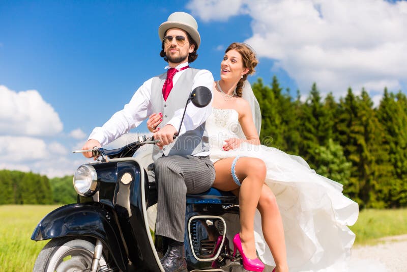 Bridal pair driving motor scooter wearing gown and suit.