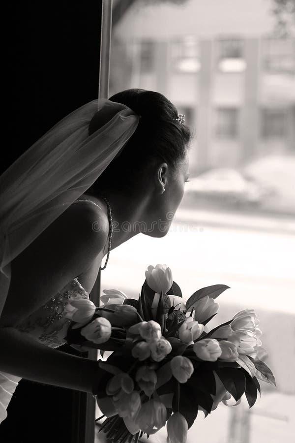 The bride with a bouquet looks out a door. b/w+sepia