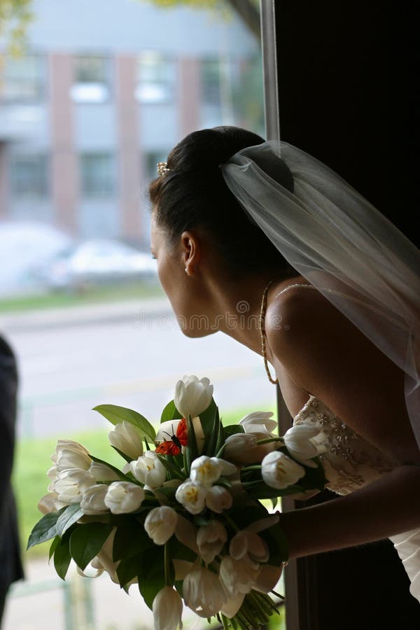 The bride with a bouquet looks out a door