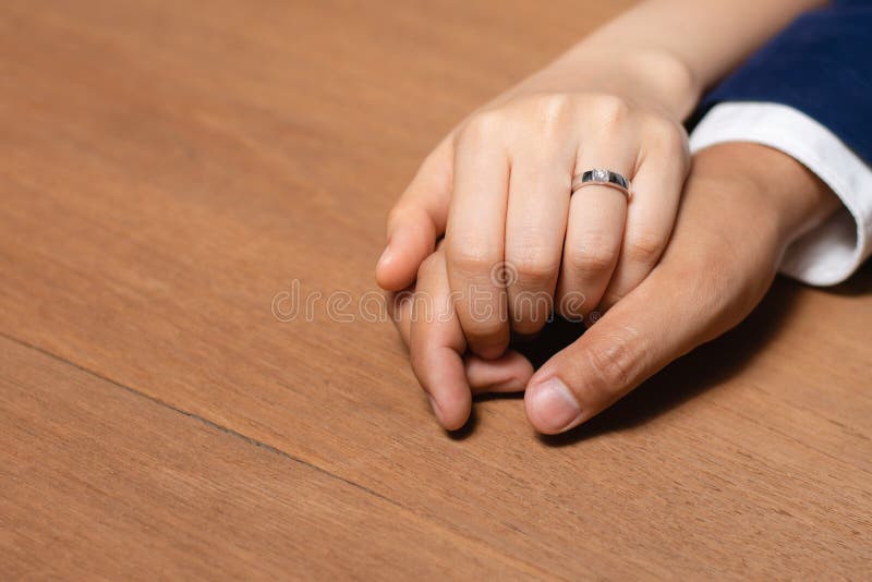 Bride and groom holding hands with wedding ring on wooden table