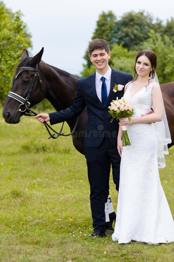 Bride and groom are standing in the park near the horse, wedding walk. White dress, happy couple with an animal. Green background