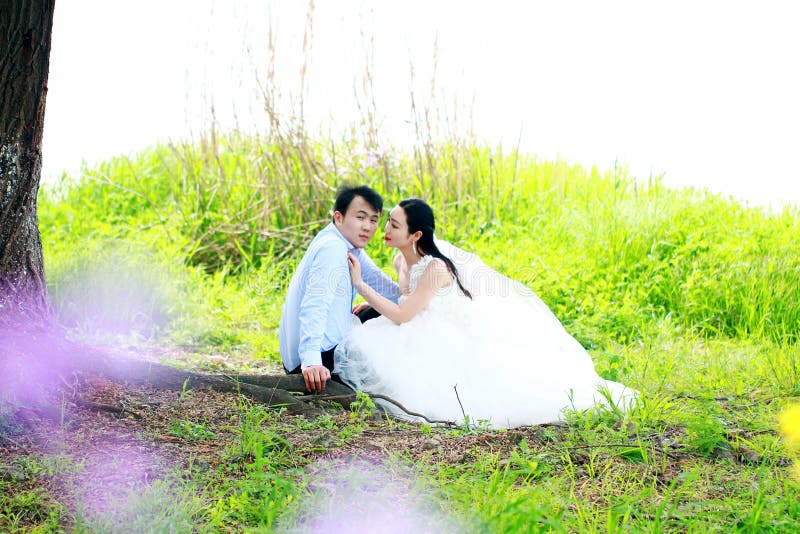 Bride and groom in wedding dress with elegant hairstyle, with white wedding dress Sitting in the grass by the river