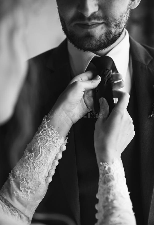 Bride Helping Groom Dressing Up for Wedding Ceremony Stock Photo