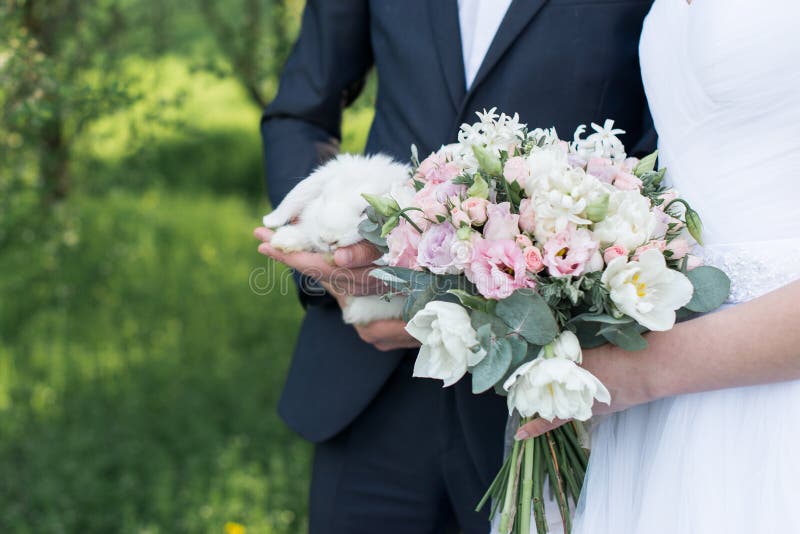 Bride holding in her hands a delicate wedding bouquet with white and pink tulips and pink small roses. Groom holding a white cute