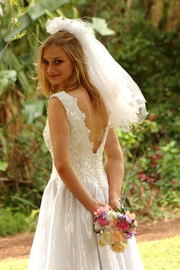 Hermoso caucásico novia feliz expresión en su lindo agotador su blanco boda ropa velo buscando de pie en jardín afuera.