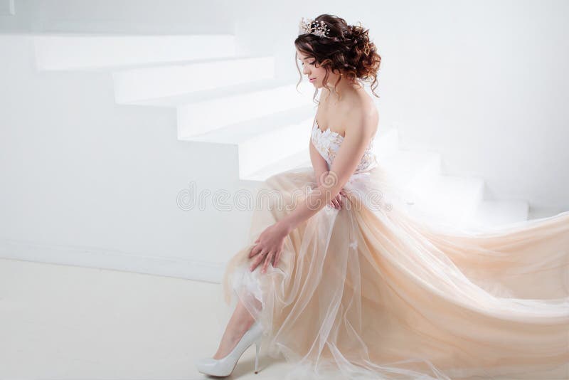 Bride sits on the stairs. Portrait of a beautiful girl in a wedding dress. Dancing Bride, white background.