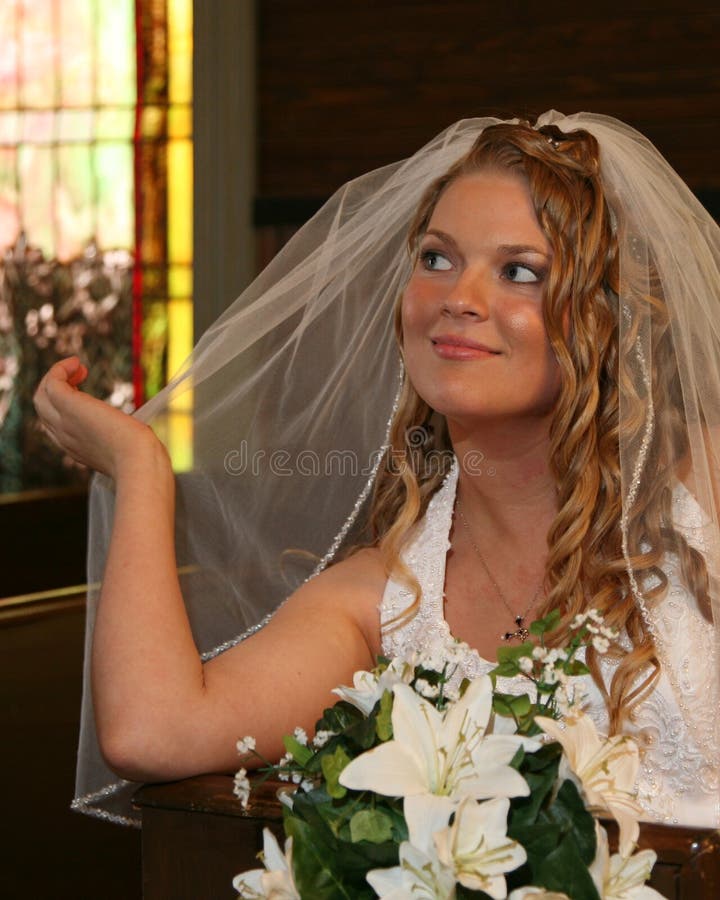 Bride sitting in a church pew holding her veil