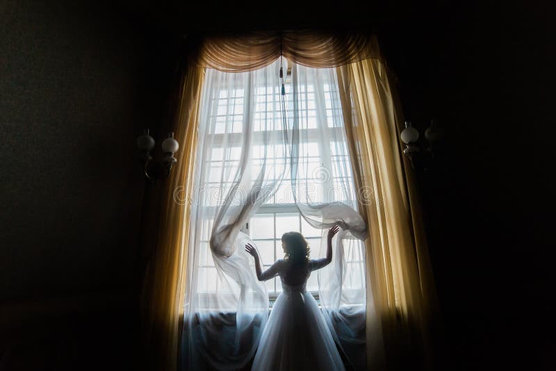The bride touches the curtains while standing near the palace window. The horizontal back view. stock photography The bride touches the curtains while standing near the palace window. The horizontal back view. stock photography
