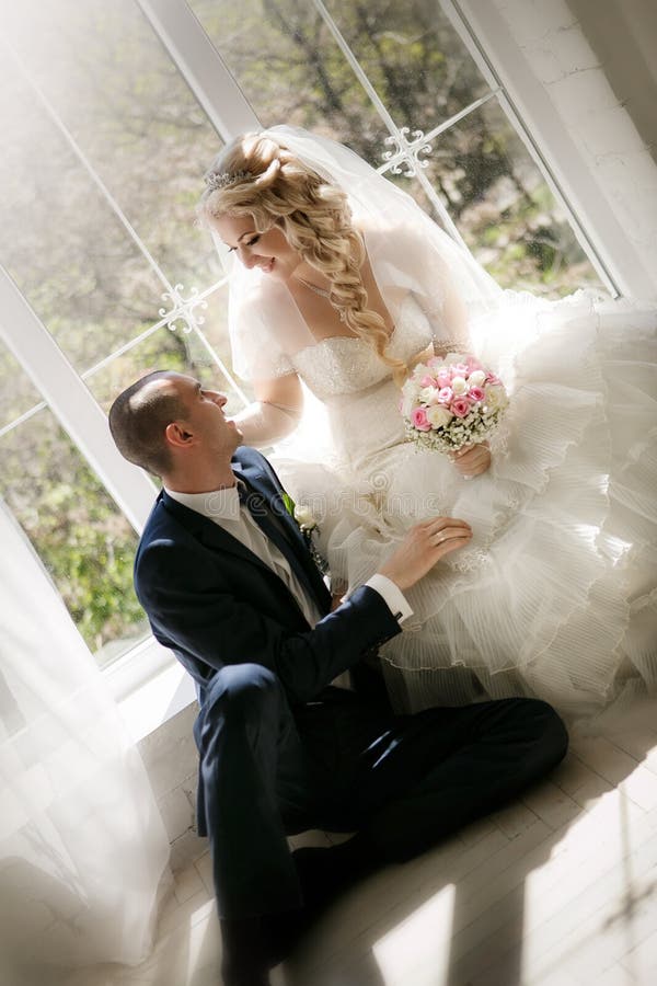 Bride with a wedding bouquet from roses and the groom sitting at a window stock image