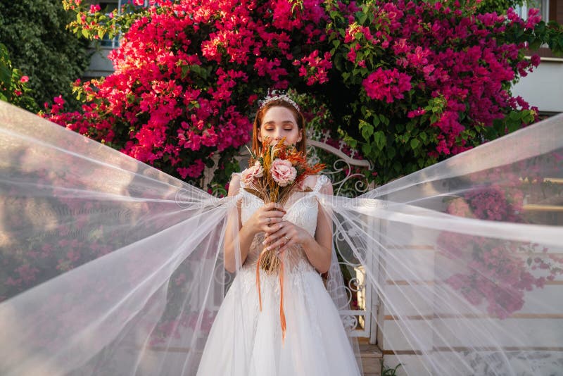 Bride with white wedding dress holding colorful and dried wedding bouquet with red bougainvillea background. stock photography Bride with white wedding dress holding colorful and dried wedding bouquet with red bougainvillea background. stock photography