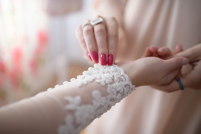 Bridesmaid or maid of honor helping the  bride buttoning up the lacy embroidered long sleeve of her dress