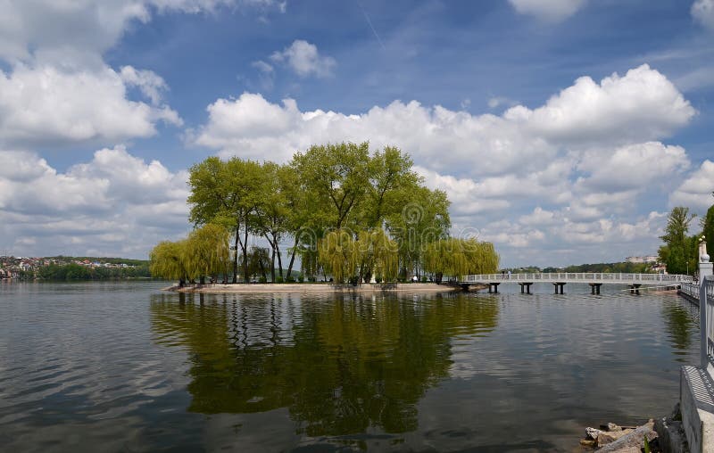 The island among the lake on which grow tall green trees against a blue sky with clouds