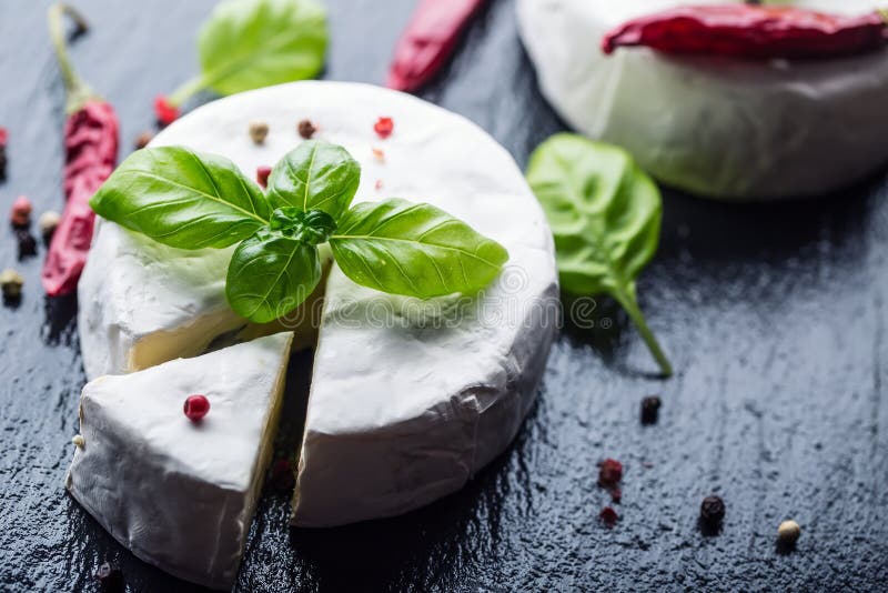 Brie Cheese Camembertkaas De verse Brie en een plak op een granietraad met basilicum verlaten vier kleuren peper en Spaanse peper royalty-vrije stock afbeelding Brie Cheese Camembertkaas De verse Brie en een plak op een granietraad met basilicum verlaten vier kleuren peper en Spaanse peper royalty-vrije stock afbeelding