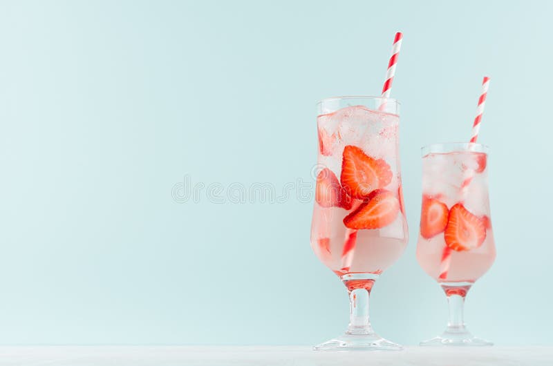 Bright cold strawberry cocktail with ripe red slices berry and sparkling water, ice cubes, red striped straw in misted glass.