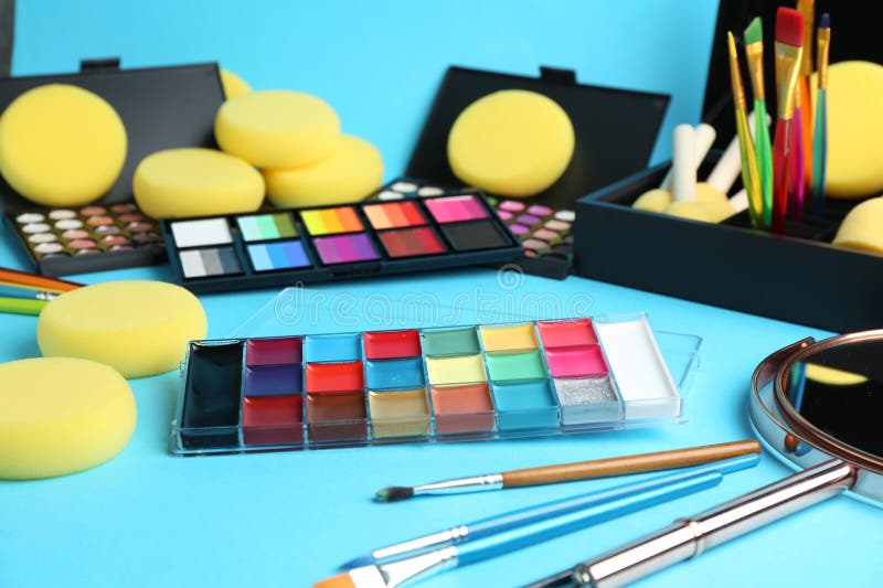 Bright face paints, brushes, mirror and sponges on light blue background royalty free stock photo