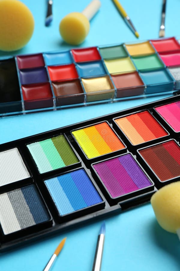 Bright face paints, brushes and sponges on light blue background, closeup stock photography