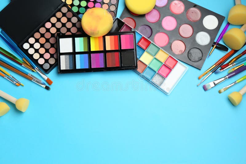 Bright face paints, brushes and sponges on light blue background, flat lay. Space for text royalty free stock photos