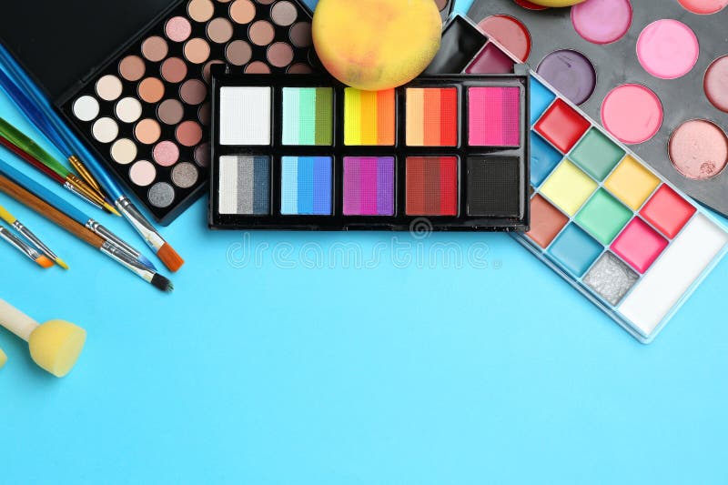 Bright face paints, brushes and sponges on light blue background, flat lay. Space for text stock image