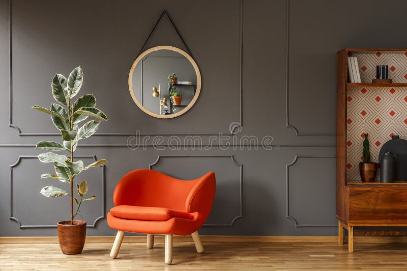 Bright orange armchair, a retro wooden cabinet and a mirror on a