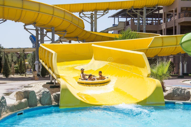 On a bright sunny day at the water park, the family slides down the hill on an air mattress stock photo On a bright sunny day at the water park, the family slides down the hill on an air mattress stock photo