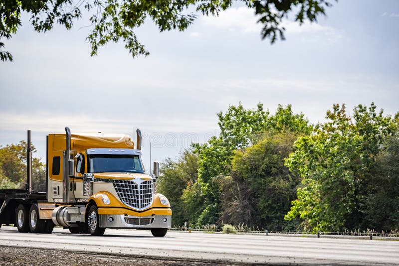 Stylish Big Rig Yellow Semi Truck with Chrome Accessories Transporting Step  Down Semi Trailer Moving on the Road with Trees on the Stock Photo - Image  of commercial, industrial: 202408212