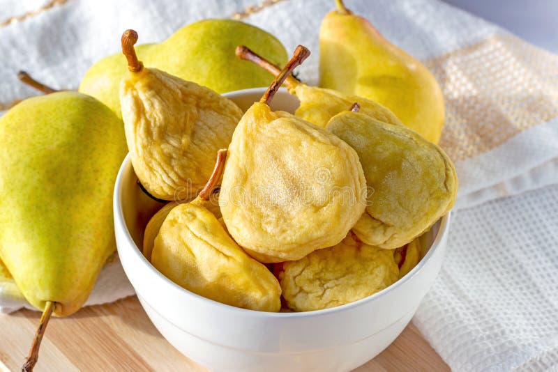 Bright yellow whole dried pears in the white bowl and fresh fruit on the wooden background stock photography Bright yellow whole dried pears in the white bowl and fresh fruit on the wooden background stock photography