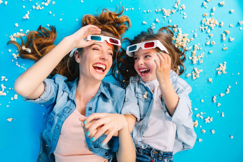 Brightful modieus beeld van hierboven opgewekte moeder en dochter die op blauwe vloer in popcorn leggen, die in 3D glazen lachen royalty-vrije stock afbeeldingen Brightful modieus beeld van hierboven opgewekte moeder en dochter die op blauwe vloer in popcorn leggen, die in 3D glazen lachen royalty-vrije stock afbeeldingen