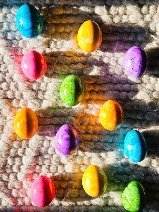 Brightly colored Easter eggs on textured wool rug in sunlight. Vibrant spring holiday backdrop stock photo