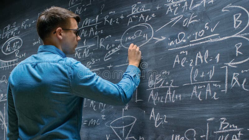 Brilliant Young Mathematician Approaches Big Blackboard and Finishes writing Sophisticated royalty free stock photos