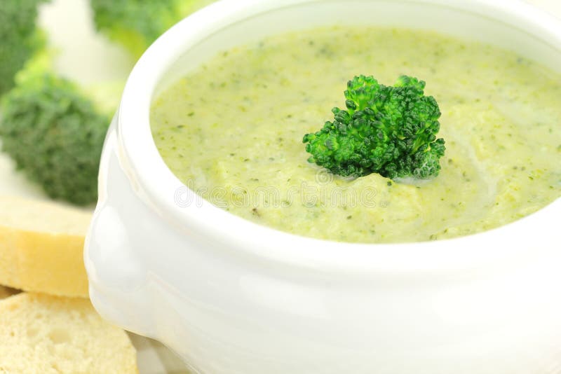 Broccoli soup. Creamy broccoli soup in a white bowl served with some bread royalty free stock photography